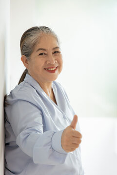 Happy smiling Asian silver generation old woman showing approving, passing, good, yes, go for it, good to go, one thumb up hand gesture, indoor scene