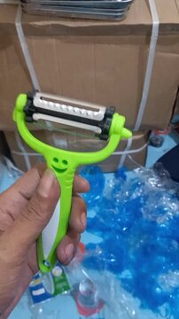 A hand holds a vibrant green razor handle in front of cardboard boxes and scattered blue items