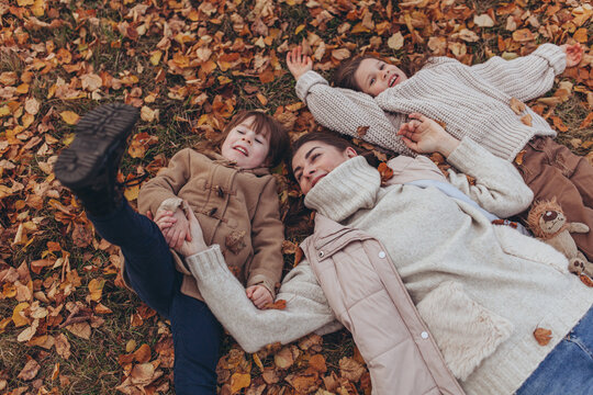 Happy mother with two daughters lying on ground with autumn leaves in park. Love, joy, childhood, family lifestyle, autumn walk.