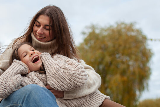 Happy mother and daughter laughing together outdoors in autumn, wearing cozy knit sweaters. Unconditional love, warmth, and joy in family relationships. Mother's day.