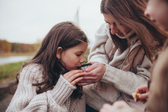 Mother and her daughter sharing warm drink from thermos cup in autumn. Family bonding, tenderness and care.