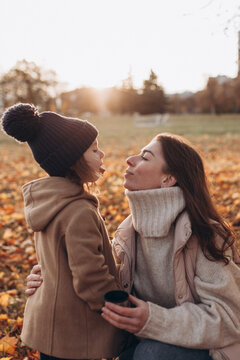 Playful moment between young mother and daughter sticking out her tongue at mom in autumn park. Family bonding, motherhood, lifestyle, parenting, crisis.