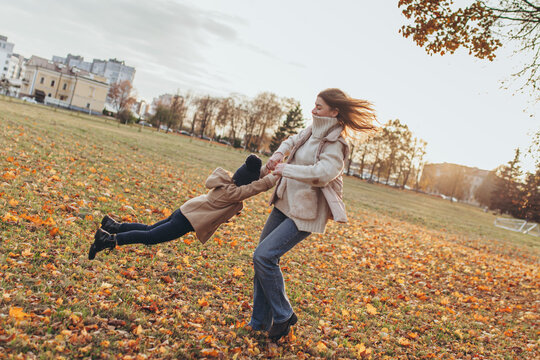 Happy mother spinning her little daughter in autumn park. Moment of happiness, family lifestyle, mother's day.