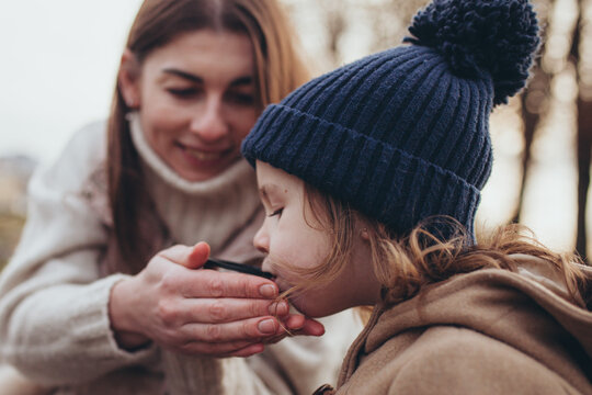 Caring mother feeding her little daughter with hot drink outdoors in autumn.Maternal care, love, and family connection during cold season. Mother's day.