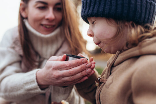Little girl squinting while drinking hot tea from mother's hands. Tender, cozy moment of parent-child bonding during cold autumn day. Care, family support, autumn lifestyle, parenting.