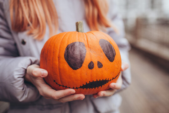 Close up of hand-painted Halloween pumpkin in girl's hands. DIY Halloween celebrations and creative holiday preparation.
