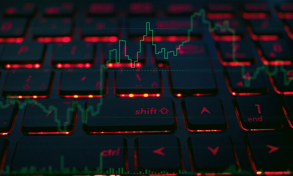 Detailed shot of red illuminated computer keyboard keys featuring an overlay of active green stock market index line charts for online day trading