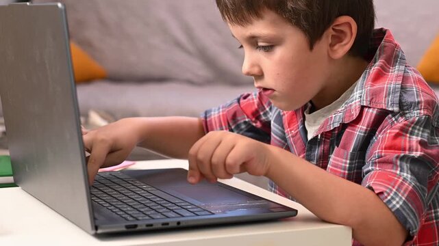 A 6-year-old boy is learning to type on a laptop and is sitting in the living room doing his homework.