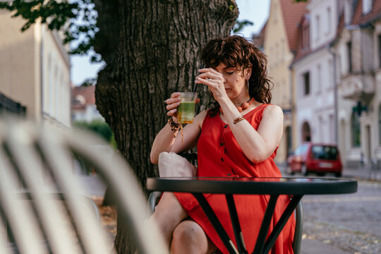 Stylish mature woman stirring iced matcha drink while relaxing at outdoor city cafe table