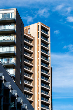 Rising in London, Isle of Dogs, England, a modern residential apartment tower carries glass balconies and a sharp facade against open blue sky.