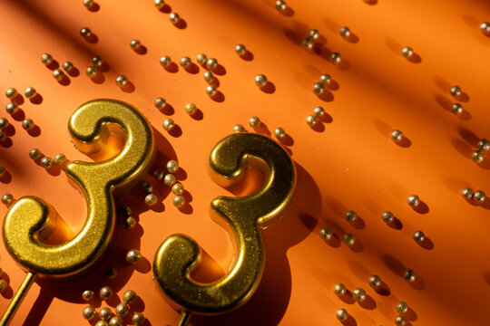 vibrant festive backdrop for 33rd birthday, made of gold candles shaped like number thirty-three, placed on an orange background with sprinkles. versatile festive banner with space for text.