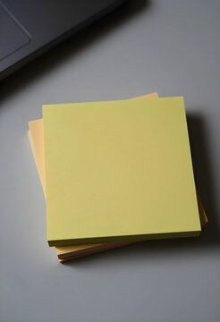Stack of blank yellow and orange sticky notes on a gray desk with a laptop corner office supplies and organization