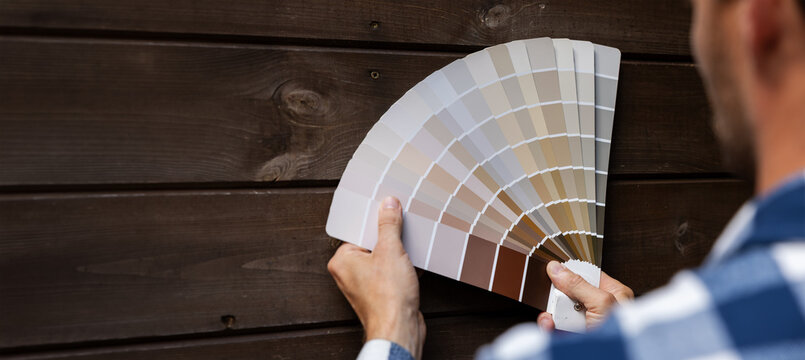 man choosing paint color from samples palette for wooden plank house exterior cladding. copy space