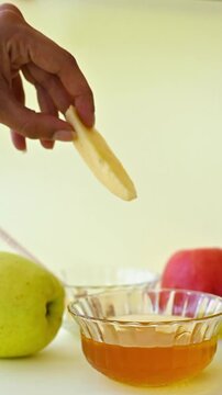 Hand Dipping Apple Slice into Glass Honey Jar for Rosh Hashanah, Jewish New Year Tradition, Shana Tova