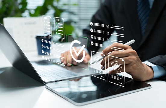 Businessman reviews digital compliance checklists on laptop and tablet, illustrating document approval, quality control, audit workflow, regulatory management, and corporate verification.