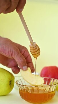 Hand Using Wooden Honey Dipper to Drizzle Honey Over Apple for Rosh Hashanah, Jewish New Year Tradition, Shana Tova