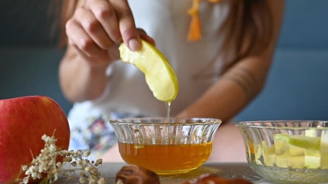 Woman's Hand Dipping Apple in Honey for Rosh Hashanah, Jewish New Year Food Tradition, Sweet Year Celebration