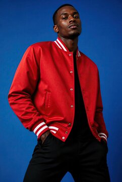 Confident Young Man Wearing Red Varsity Jacket Posing Against Vibrant Blue Background in Studio