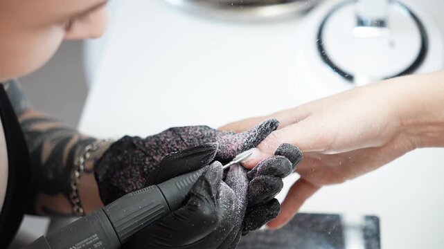 Nail technician removes old nail polish from a client's fingernail using an electric nail drill. Professional manicure, nail care and beauty salon service concept