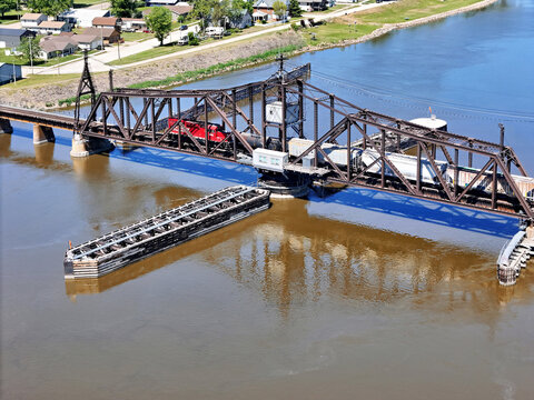 Aerial view of a railroad swing bridge with freight train crossing over reflective river in small Midwestern town