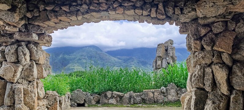 Stone archway framing lush green hills and cloudy mountains landscape