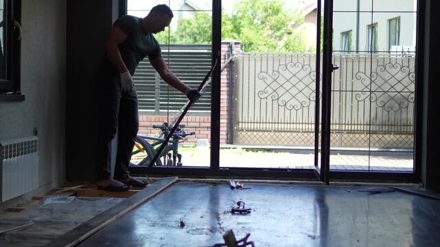 A cinematic medium shot of a strong man using a heavy crowbar tool to rip up old wooden floorboards during a home renovation project. 
