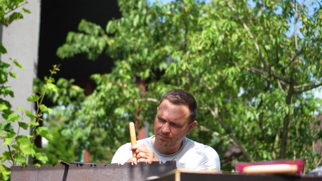 A close-up shot of a focused man peeling a long sausage before grilling it over a barbecue, depicting funny preparation and backyard cooking.