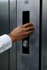 Naklejka premium Person in white shirt reaching for a modern elevator call button on a brushed metal panel, close up