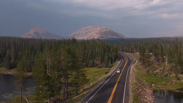 Aerial of winding road and Bald Mountain through Uinta Wasatch Cache National Forest with lakes with dense coniferous forest lining the route