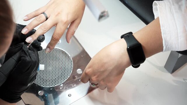 Nail technician removes cuticle from a client's fingernail using an electric nail drill. Professional manicure, nail care and beauty salon service concept