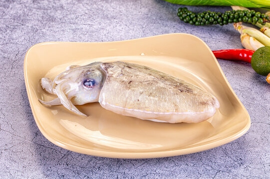 Fresh cuttlefish on beige plate with green peppercorns and red chili