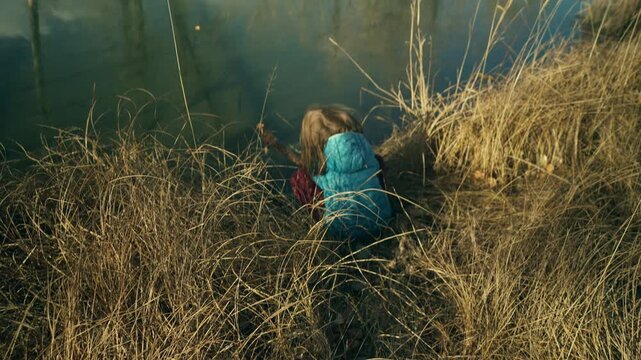 Boy crouches among tall dried grass at the edge of a frozen river in winter