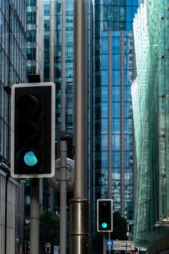 Between reflective towers, a green traffic signal appears against glass as the facade lines a street in London, England, compressing urban architecture into depth.