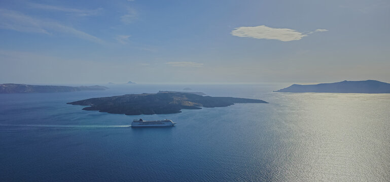 High panoramic aerial view of luxury cruise ship sailing in deep blue Aegean sea caldera near Nea Kameni volcanic island in Santorini archipelago Greece