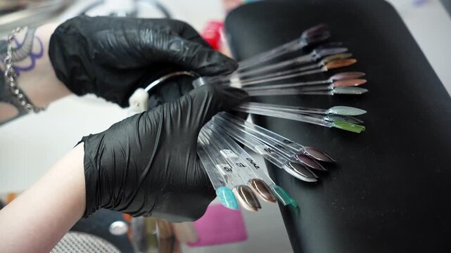 Nail technician compares colorful nail samples while choosing a gel polish shade. Professional manicure, color selection and beauty salon service concept