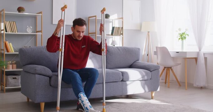 Adult man with broken leg trying to walk with cruthes, has bone fracture, has long period of rehabilitation and making good progress, spending time at home. Orthopedic problems concept
