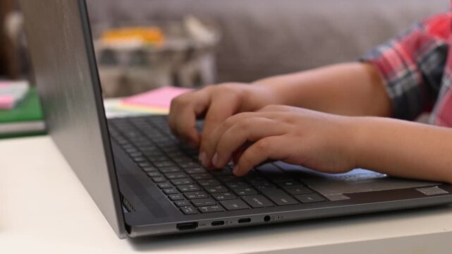 6 year-old boy sitting in living room, learning to type on notebook doing homework. Young child focused on computer screen, Elementary school student studying independently indoors, at home