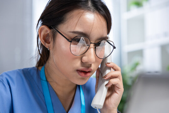 Nurse, phone, glasses, woman, medical, uniform, clinic Asian health worker speaking on telephone with focused expression in bright office workspace