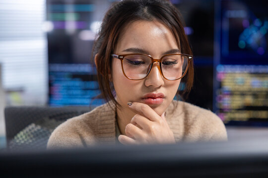 Asian woman programmer computer eyeglass office code screen thoughtful technology work, Asian woman wearing eyeglass working computer office with code screen, thoughtful expression, technology