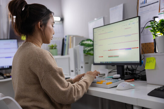Woman office computer monitor keyboard desk typing workspace technology business, female worker typing at desk with monitor and keyboard in modern office workspace, focused calm expression