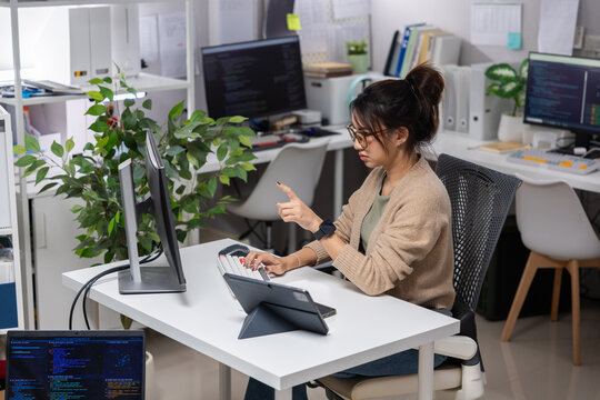 Woman office tablet computer desk stylus workspace programmer technology plant, focused woman using stylus tablet beside computer modern desk bright office workspace with code screen and indoor