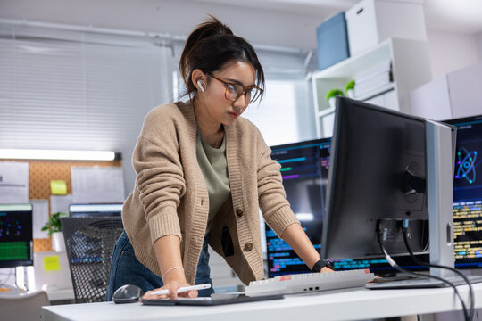 Female programmer office computer monitor keyboard glasses code technology workstation software developer working at desk with focused expression in modern office workspace