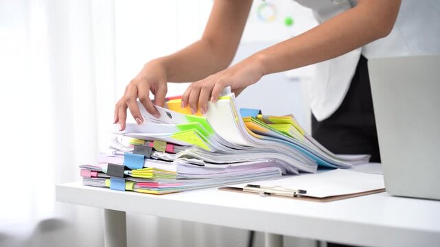 Businesswoman hands working in Stacks of paper files for searching and checking unfinished document achieves on folders papers at busy work desk office.	