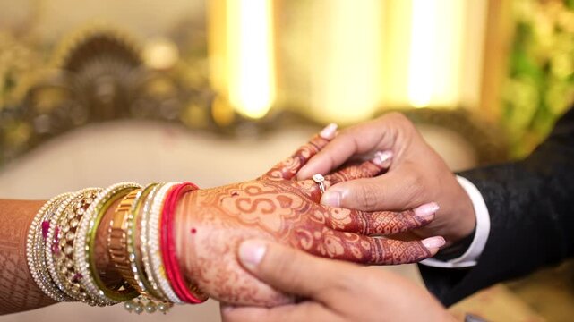 Groom putting engagement ring on bride hand with henna design at Indian wedding ceremony