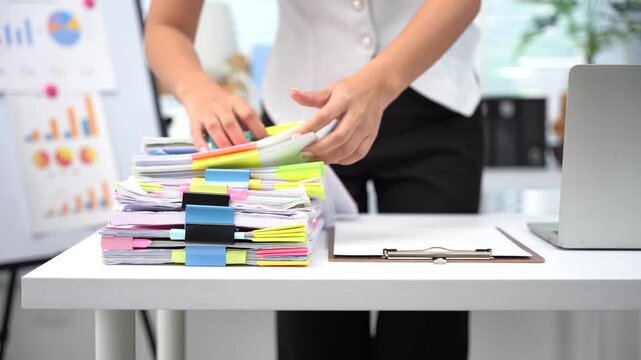Businesswoman hands working in Stacks of paper files for searching and checking unfinished document achieves on folders papers at busy work desk office.	