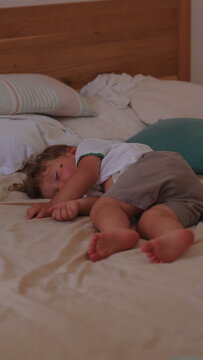 Toddler sleeping peacefully on bed at home, briefly brushing away fly while remaining asleep, capturing deep rest, natural behavior and authentic childhood