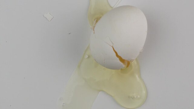 Slow motion. chicken egg breaks from falling onto white table, top view. egg falls to the surface and breaks.