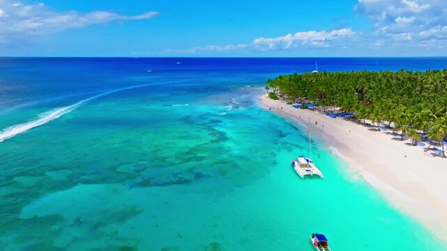 An aerial view of a luxury beach vacation on the Caribbean palm-lined coast. Drone view of a tropical resort beach in the Dominican Republic on a sunny day. Boats and yachts off the coast.