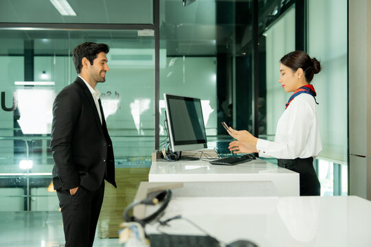 Customer service staff helps a traveler at an airport counter while using a mobile phone to support communication and deliver convenient passenger service.

