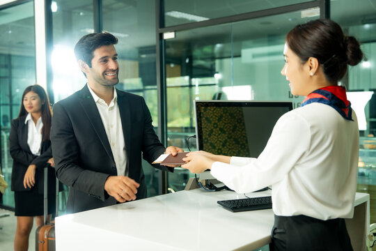 Airport personnel serves a business traveler at the check-in counter while handling travel documents and preparing the passenger for departure.